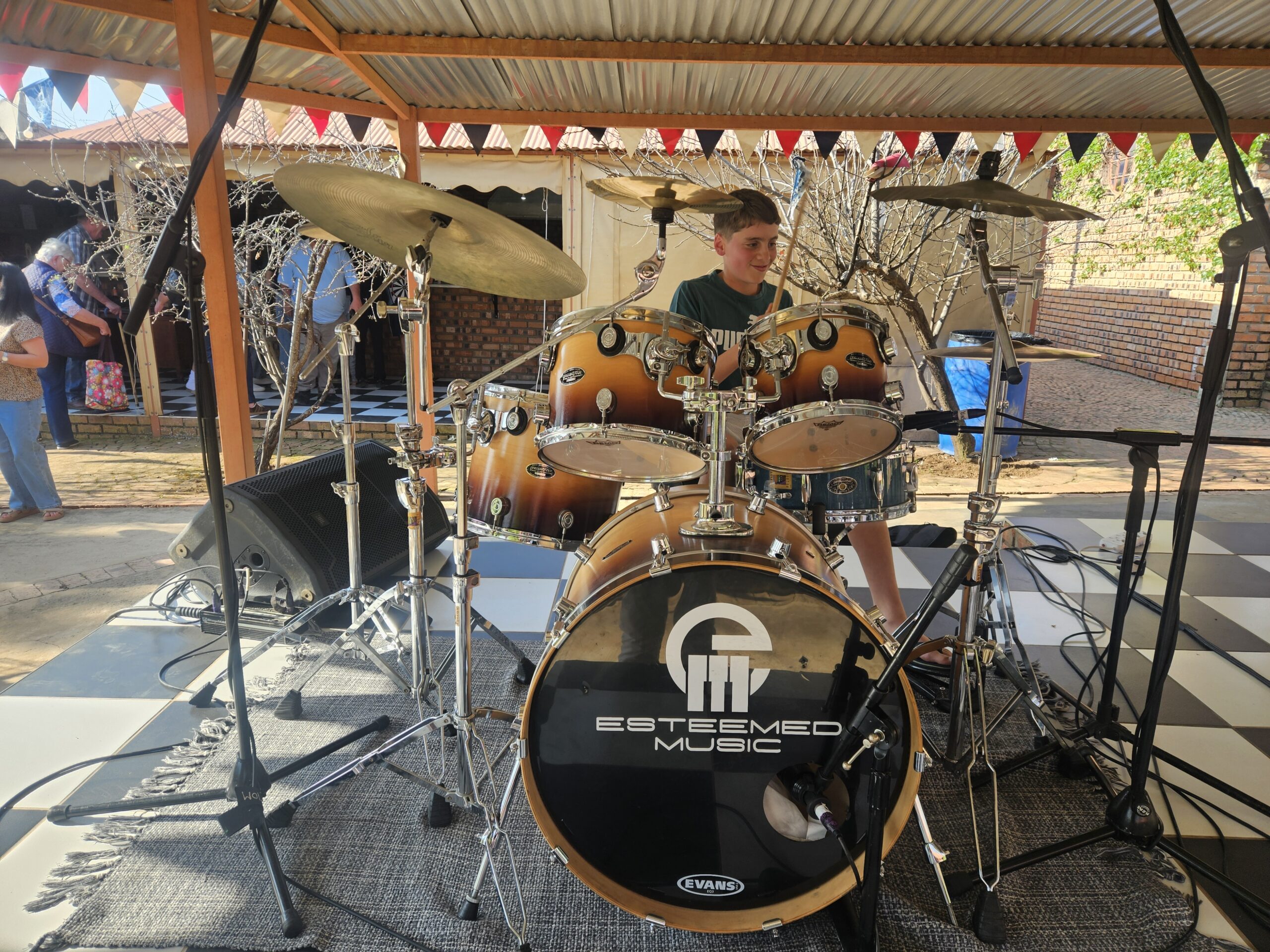 Young student playing Esteemed Music branded drum kit outdoors