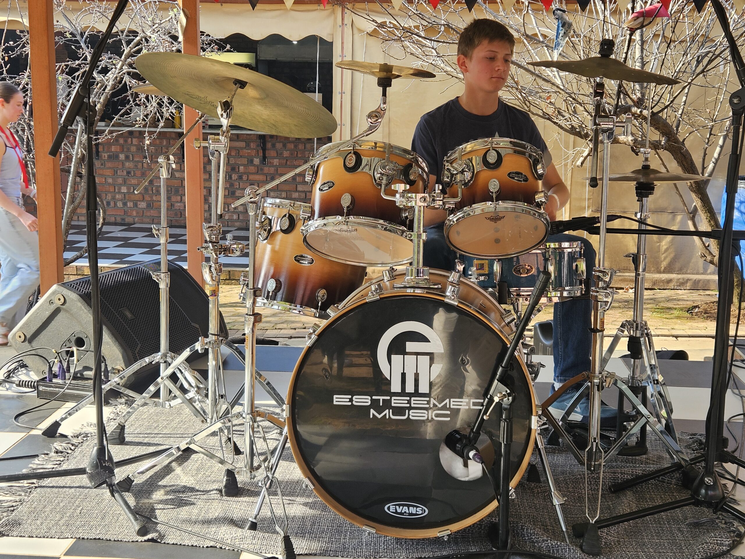 Older student playing Esteemed Music branded drum kit outdoors